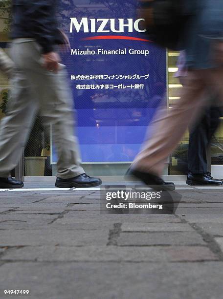 Pedestrians walk past the Mizuho Financial Group Inc. Logo displayed outside the company's headquarters in Tokyo, Japan, on Thursday, April 23, 2009....