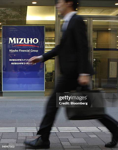 Man walks past the Mizuho Financial Group Inc. Logo displayed outside the company's headquarters in Tokyo, Japan, on Thursday, April 23, 2009. Mizuho...