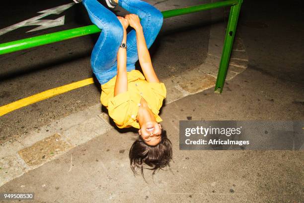 young woman hanging upside down from a railing in the city at night. - upside down stock pictures, royalty-free photos & images