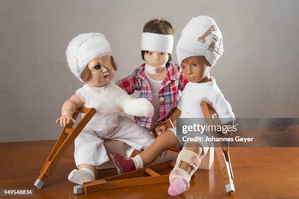 three dolls sitting, bandages on head, leg splint, crutches, eye patch, arm and shoulder bandage, neck brace - medical eye patch stockfoto's en -beelden