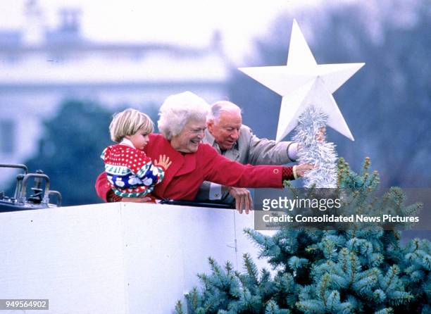 In a cherrypicker, First Lady Barbara Bush holds her grandson, Walker Bush, as she and American banking executive Joseph H Riley place a star...