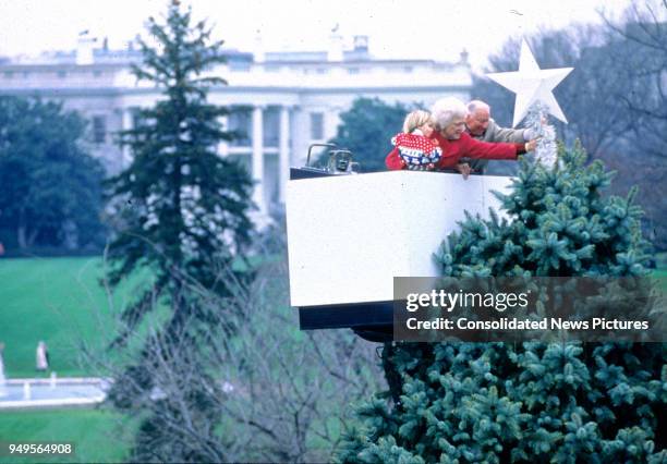 In a cherrypicker, First Lady Barbara Bush holds her grandson, Walker Bush, as she and American banking executive Joseph H Riley place a star...