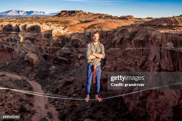 sportlicher junger mann posiert auf einer highline oder slackline in moab utah - tightrope walking stock-fotos und bilder