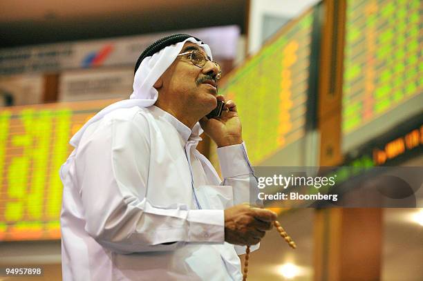 An investor checks the stock markets while talking on his mobile phone on the floor at the Dubai Financial Market, at the Dubai World Trade Centre,...