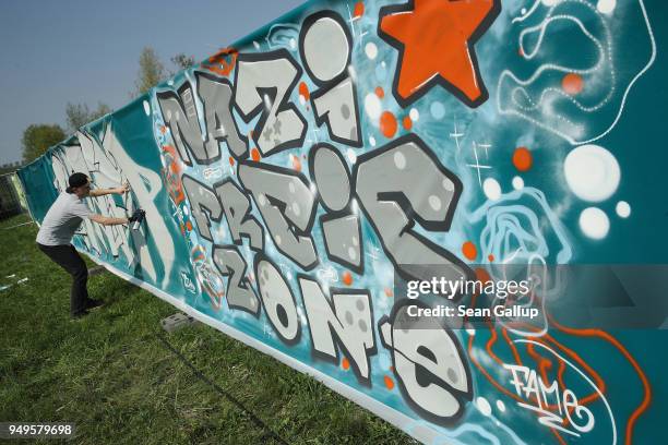 Graffiti artist sprays a barrier next to other graffiti that reads: "Nazi-Free Zone" at a leftist counter music fest not far from a neo-Nazi music...