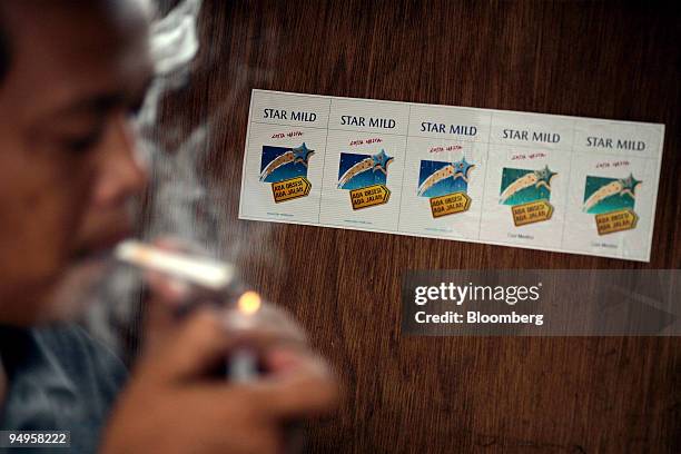Mahpud lights a cigarette in front of an advertisement for PT Bentoel Internasional Investama's Star Mild brand of kretek, or clove-flavored...