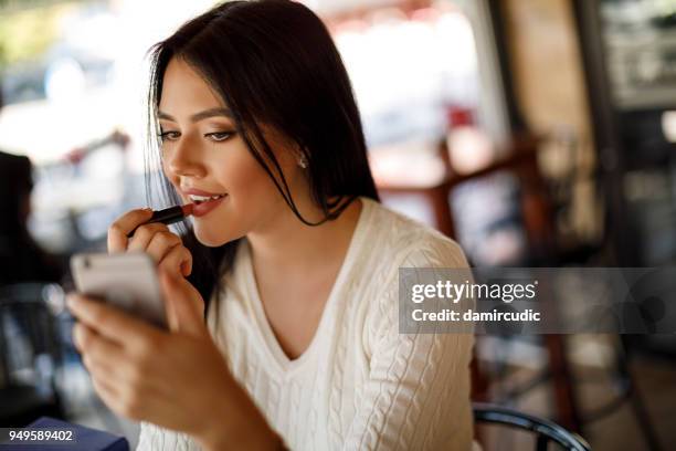 young woman applying lipstick at a cafe - acabamento mate imagens e fotografias de stock