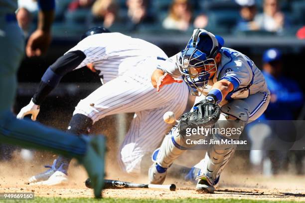 Luke Maile of the Toronto Blue Jays commits a fielding error as he can't hold onto the ball as Aaron Judge of the New York Yankees scores in the...
