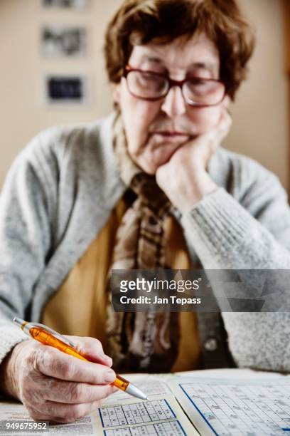 senior sits at the table at home and solves puzzles, sudoku, crossword puzzles, cologne, north rhine-westphalia, germany - crossword stock pictures, royalty-free photos & images