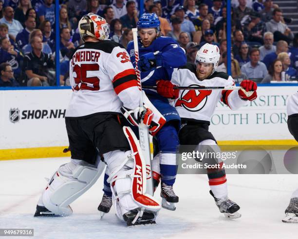 Brayden Point of the Tampa Bay Lightning is taken down from behind by Ben Lovejoy and in front of goalie Cory Schneider of the New Jersey Devils in...