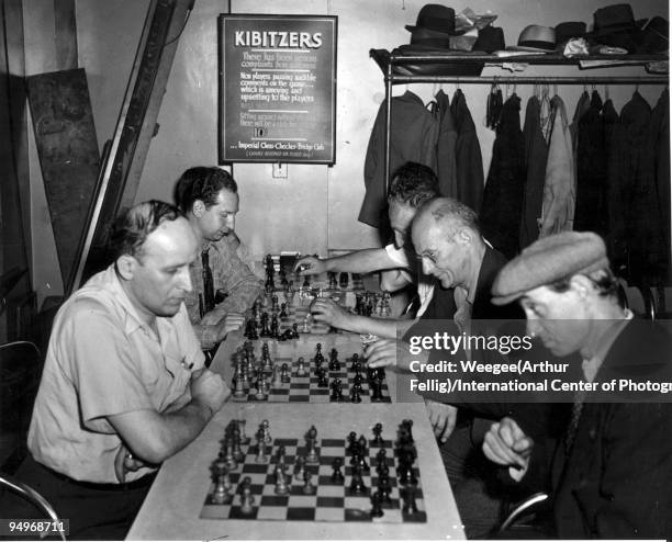 Men playing chess, in the background is a sign that reads: "Kibitzers...non players passing audible comments on the game...Imperial Chess Checker...