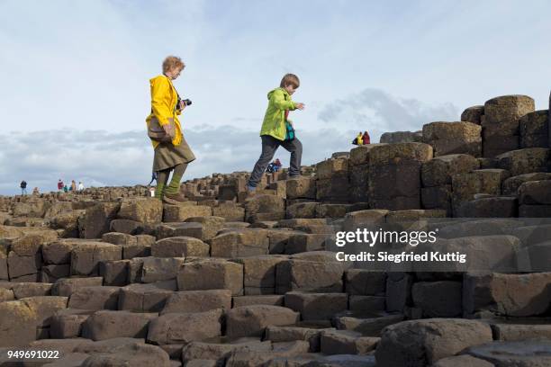 tourists walk on the basalt columns, giants causeway, causeway coast, county antrim, northern ireland, great britain - giant's causeway stock pictures, royalty-free photos & images