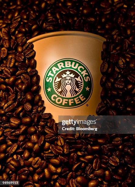 Starbucks coffee cups and coffee beans are arranged for a photograph in New York, U.S., on Tuesday, July 21, 2009. Starbucks Corporation is scheduled...