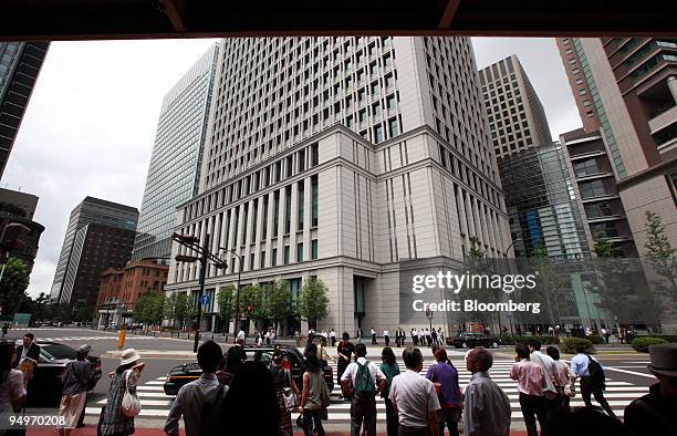 Pedestrians wait to cross an intersection in front of the building which houses the Hitachi Ltd. Headquarters, center, in Tokyo, Japan, on Monday,...