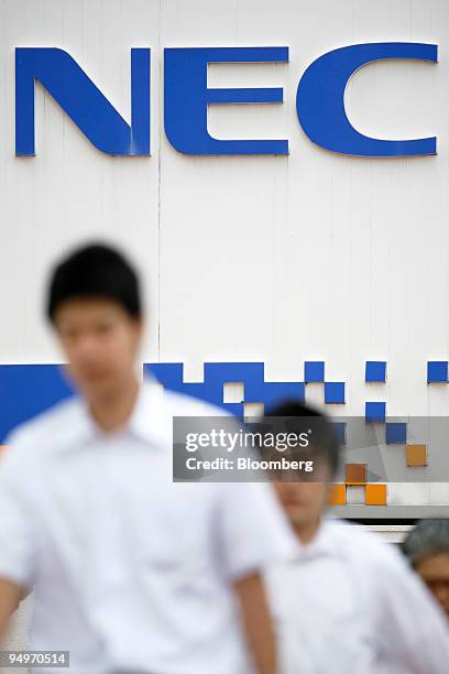 People walk in front of a sign for NEC Corp. Near the company's headquarters in Tokyo, Japan, on Thursday, July 30, 2009. NEC Corp., Japan's largest...