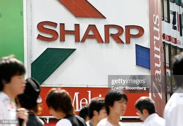 People walk past an advertisement for Sharp Corp. At an electronics store in Tokyo, Japan, on Thursday, July 30, 2009. Sharp Corp., Japan's largest...