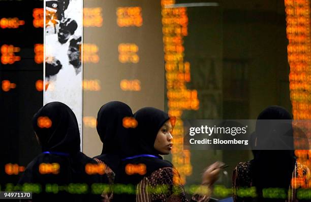 University students touring the Indonesia Stock Exchange walk past stock quotes reflected in a window in Jakarta, Indonesia, on Tuesday Aug. 18,...