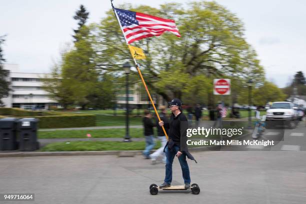 Man on a motorized skateboard carrying flags rides along the Washington State Capitol mall during a "March For Our Rights" pro-gun rally on April 21,...