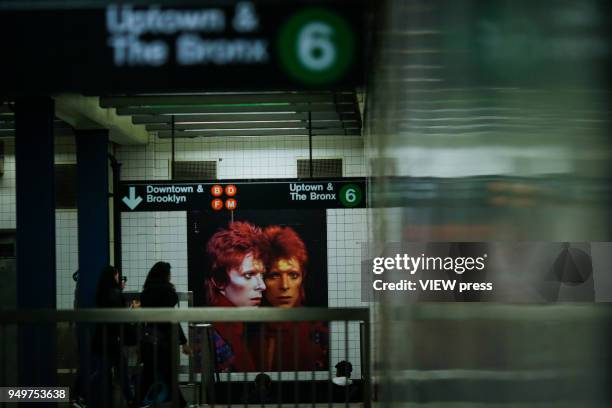 People walk at a subway station while images of David Bowie are displayed as art installations on April 20, 2018 in New York, NY. A Bowie exhibition...