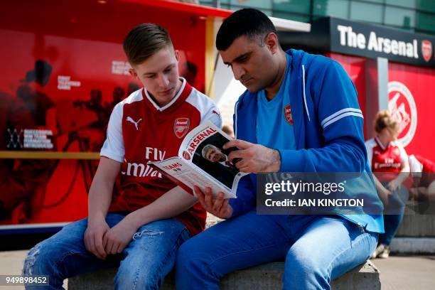 Fans read a match-day programme with a picture on Arsenal's French manager Arsene Wenger on the front during the English Premier League football...