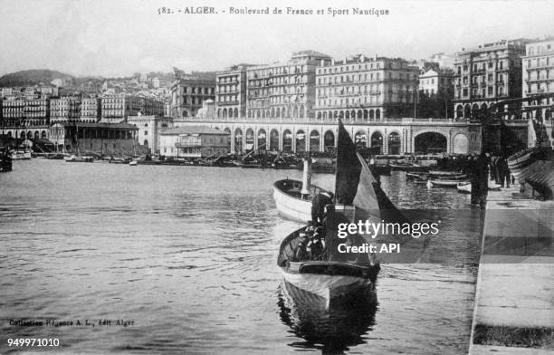 Carte postale coloniale de canotiers dans le port devant le boulevard de France au début du 20ème siècle à Alger, Algérie.