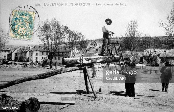Deux hommes sciant un tronc d'arbre selon une technique aveyronnaise en France.