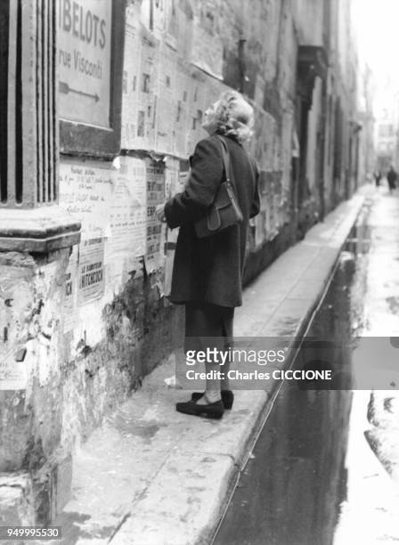 Femme agee lisant les affiches placard?es sur le mur dans le quartier de Saint-Germain-des-Pr?s, non loin de la rue Visconti, circa 1960 a Paris,...