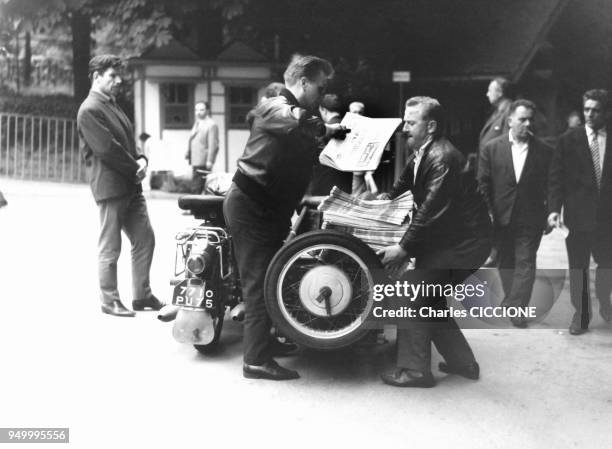Deux hommes livrent a moto le journal 'Dimanche Turf' a l'hippodrome, circa 1960 a Paris, France.