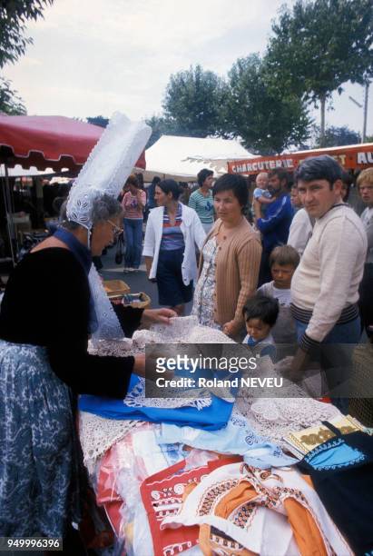 Une femme portant une coiffe bigoudène vendant des articles en dentelle sur un marché en août 1977 à Saint-Malo, France.