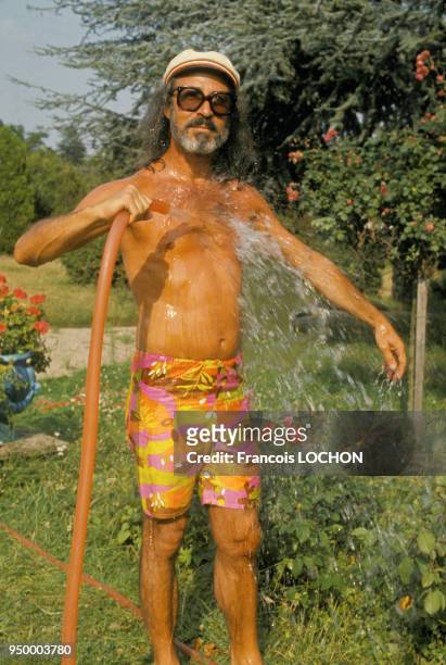 Portrait de Fernand Legros, marchand de tableaux et faussaire, en bermuda s'arrosant avec le jet d'eau d'un tuyau d'arrosage dans son jardin, en...