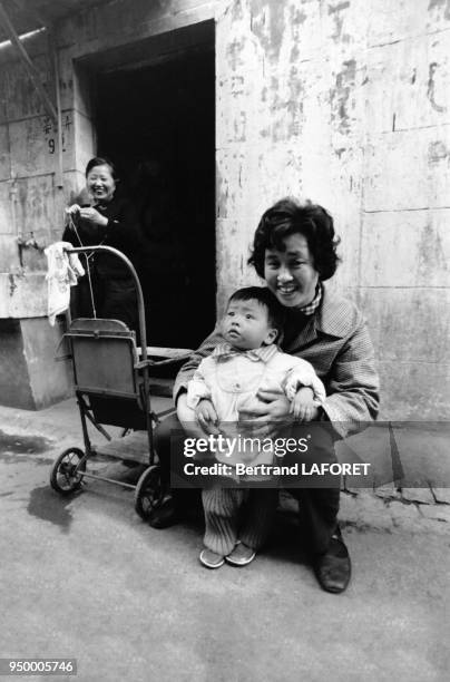 Une mère assise dans une rue tenant son enfant devant elle en février 1982 à Shanghai, Chine.