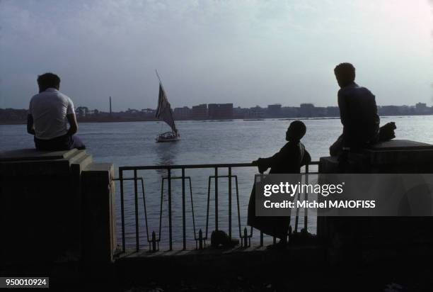 Hommes devant le Nil et bateau à voiles en avril 1980 au Caire en Egypte.