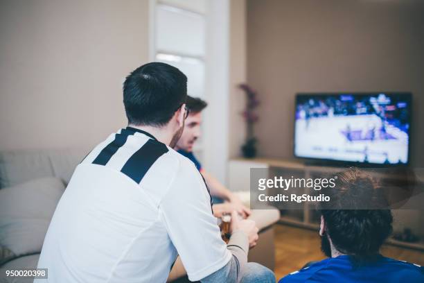 gens en maillots de sport devant la télé à la maison - friendly match photos et images de collection