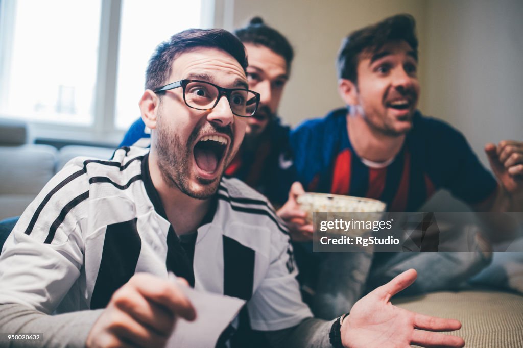 Man shouting and watching soccer game with friends with betting slip in his hand