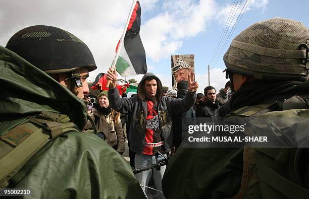Israeli soldiers stand guard opposite Palestinian protestors flashing the victory sign and waving the Palestinian flag during a demonstration against...