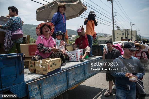 Woman reacts to the camera as she hands out free bottles of water to pilgrims walking ahead of a sedan chair holding a statue of the goddess Mazu as...