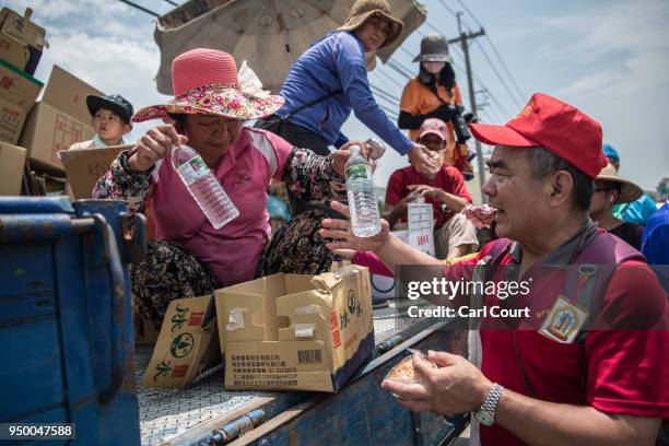 Woman hands out free bottles of water to pilgrims walking ahead of a sedan chair holding a statue of the goddess Mazu as they approach Jenn Lann...