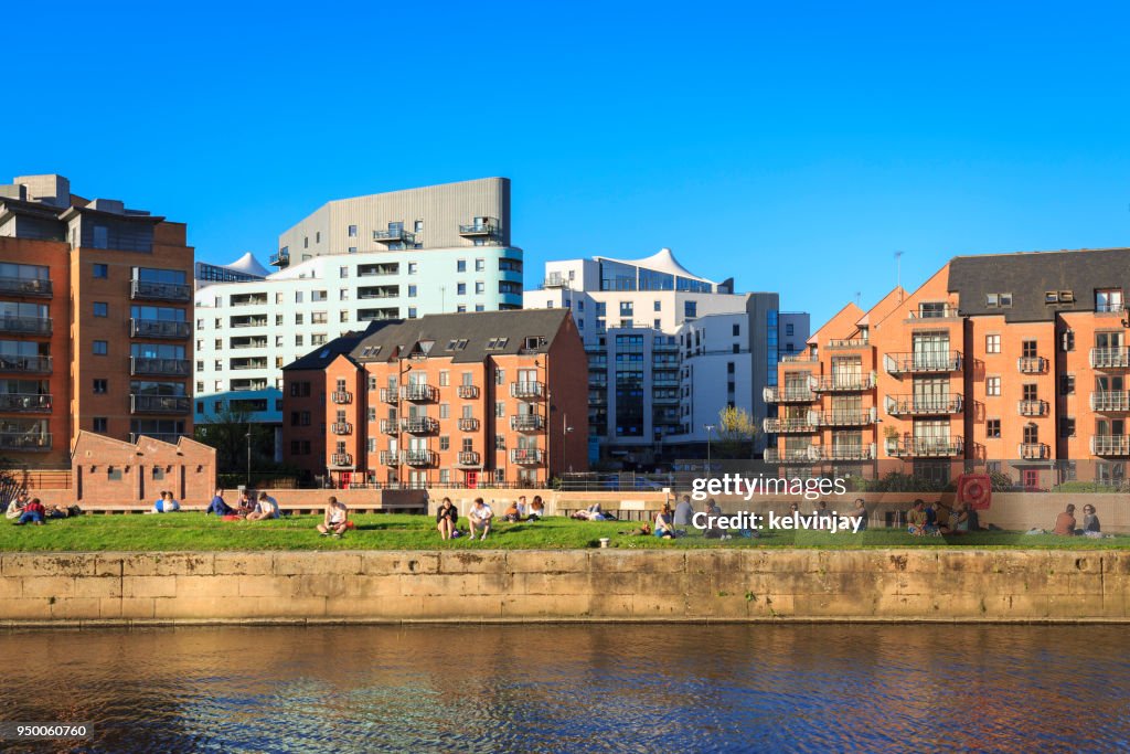 People enjoying the sunshine near apartments by the river Aire in Leeds, Yorkshire.