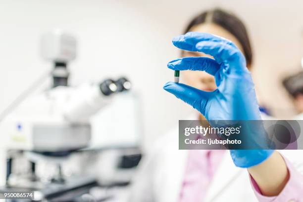joven atractivo científico femenino sosteniendo una píldora - fábrica farmacéutica fotografías e imágenes de stock