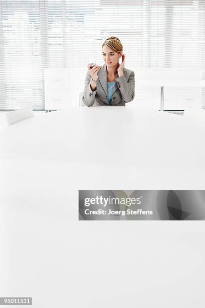 businesswoman looking into compact mirror at conference room table - compact mirror stockfoto's en -beelden