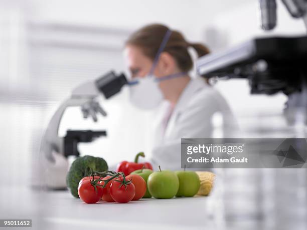 fruits and vegetables next to scientist using microscope - voedselveiligheid stockfoto's en -beelden