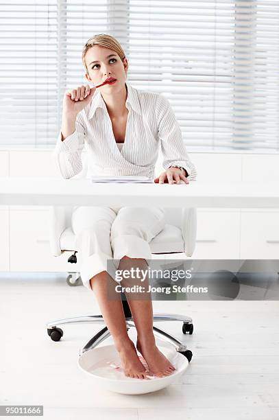 businesswoman soaking feet under desk - businesswoman barefoot stock-fotos und bilder