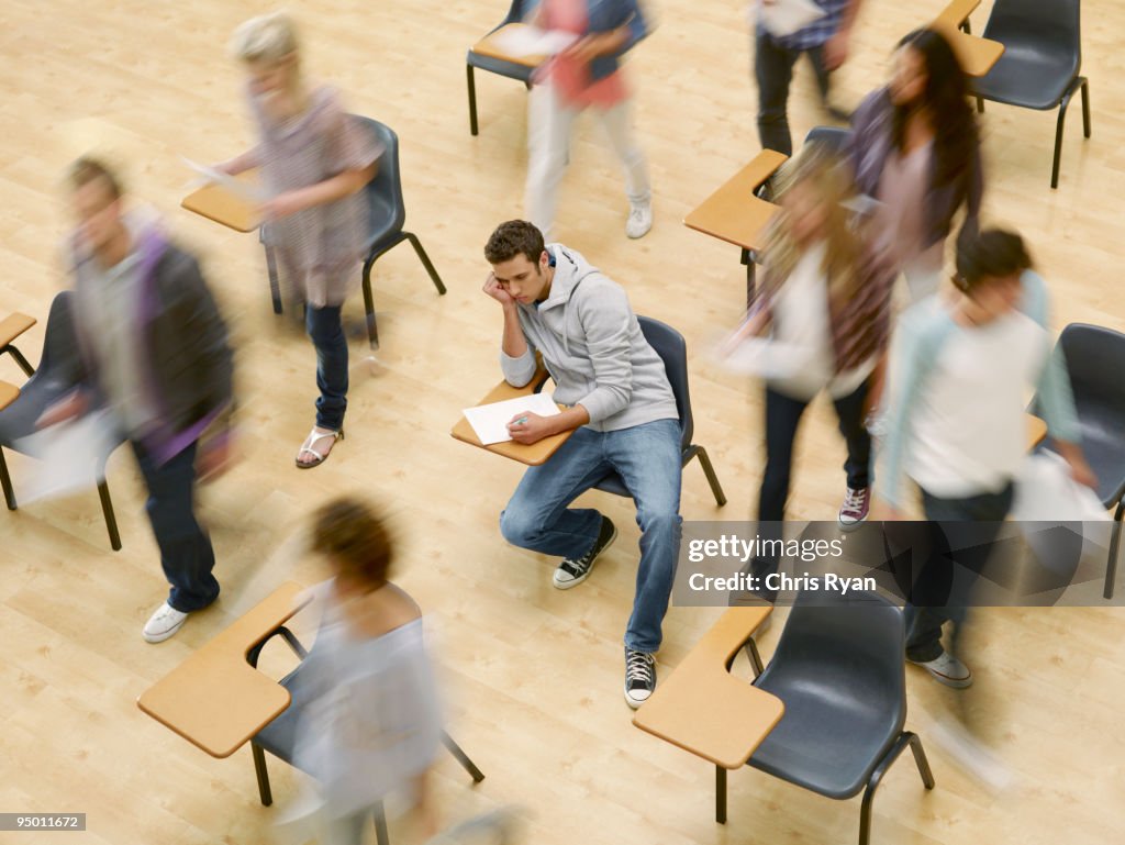 College students moving around man at desk in classroom