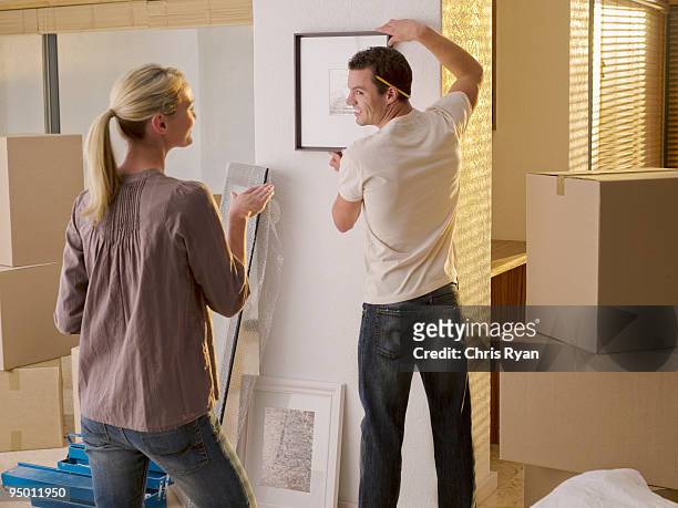 couple hanging picture in new house - three quarter length stock pictures, royalty-free photos & images