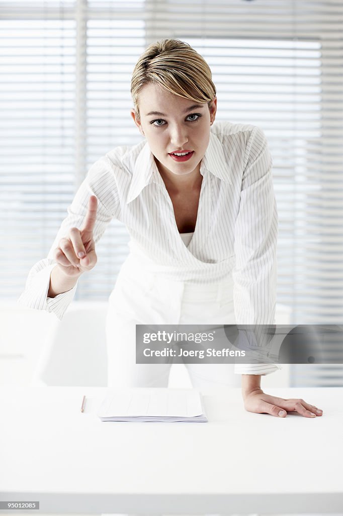 Businesswoman leaning on desk and gesturing with finger