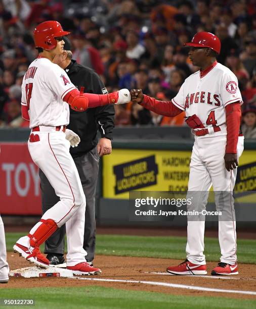 Shohei Ohtani gets a fist pump from first base coach Alfredo Griffin of the Los Angeles Angels of Anaheim after a single in the game against the San...