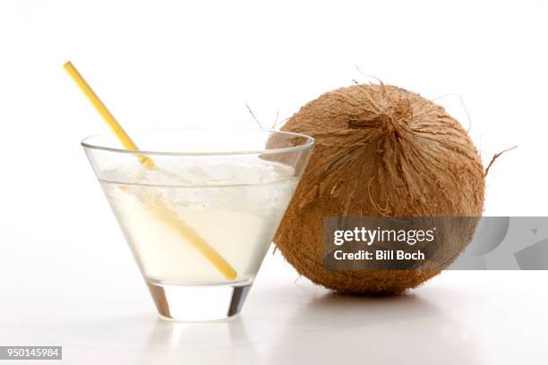 glass of coconut water with ice, a straw, and a whole coconut next to it on a white background - coconut water stock pictures, royalty-free photos & images
