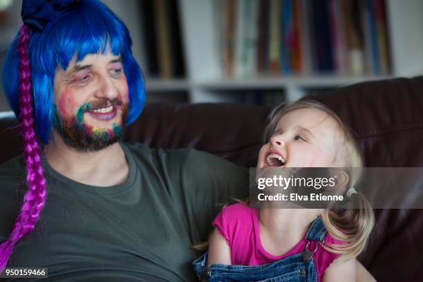 carefree adult male wearing blue wig and makeup, laughing with child (4-5) - quirky family stockfoto's en -beelden