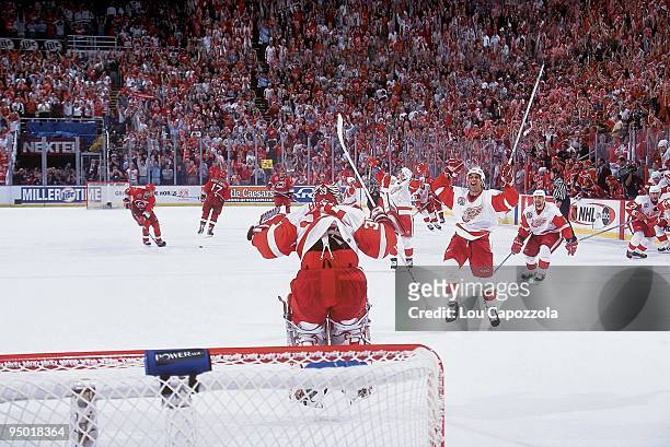 Rear view of Detroit Red Wings goalie Dominik Hasek victorious, jumping in air as teammate Chris Chelios skates onto ice with team after winning Game...
