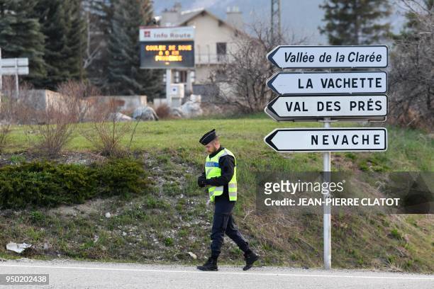 French gendarme walks by a road sign at the entrance to the valley of Nevache on April 23, 2018 near Briancon, southeastern France, a route leading...